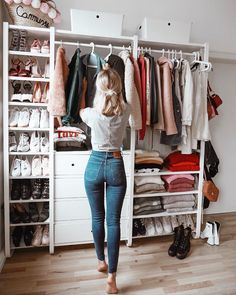 a woman standing in front of a closet full of clothes and shoes, looking into the closet