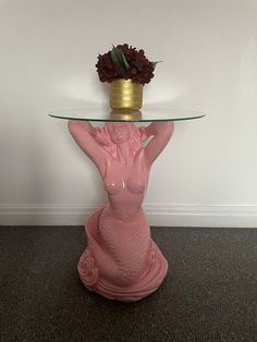 a glass table with a vase on top of it and a mermaid figure sitting underneath