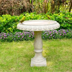 a bird bath sitting on top of a lush green field in front of some bushes