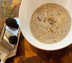 a white bowl filled with soup next to two blackberries on a wooden table top