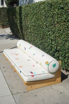 a white couch sitting on top of a wooden bench next to a lush green hedge