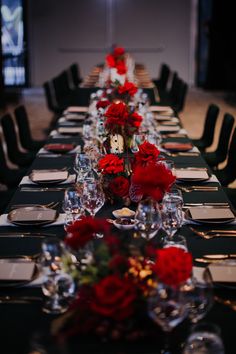 a long table is set with red flowers and place settings for the dinner guests to sit at