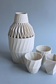 three white vases sitting next to each other on a blue surface with one empty cup in the foreground