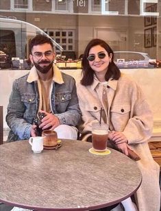 a man and woman sitting at a table with cups of coffee in front of them