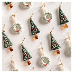 many christmas tree ornaments are hanging from hooks on a white surface with gold ear wires