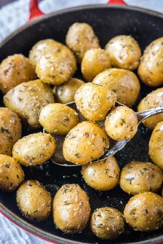 a pan filled with cooked potatoes on top of a white table cloth next to a metal spoon