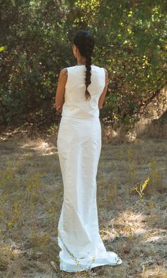 a woman in a white dress is walking through the grass with her back to the camera