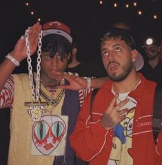 two young men standing next to each other with chains on their neck and hands in the air