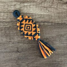 an orange, black and white beaded brooch with tassels sits on a wooden surface