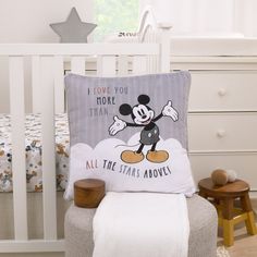 a mickey mouse pillow sitting on top of a chair next to a baby crib