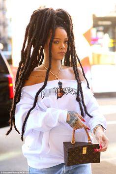 a woman with dreadlocks is walking down the street holding a purse and looking at her cell phone