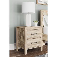 a nightstand with two drawers and a white lamp on top of the night stand next to a bed