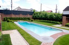 an empty swimming pool in the middle of a yard with green grass and brick edging