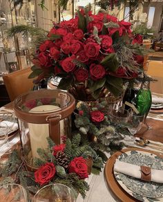 a table set for christmas with red roses and greenery on the centerpieces