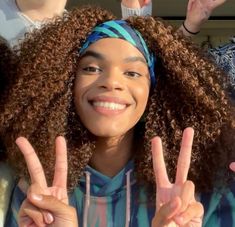 a woman with curly hair making the peace sign in front of other people holding up their hands