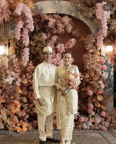 two people standing next to each other in front of a floral wall with flowers on it