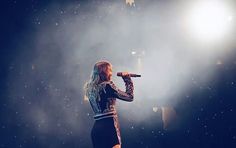 a woman standing on top of a stage with a microphone in her hand and lights behind her