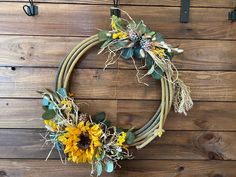 a wreath with sunflowers and greenery hanging on a wooden wall