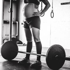 a pregnant woman standing in front of a barbell with her hands on her hips