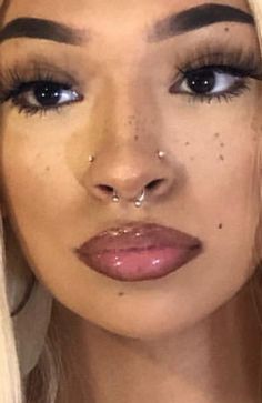 a close up of a person with long blonde hair and piercings on her nose