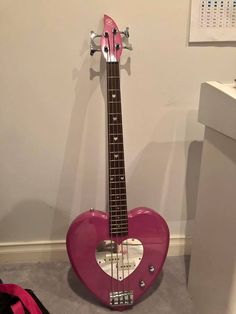 a pink heart shaped guitar sitting on the floor