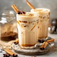 two glasses filled with ice cream and cinnamon on top of a table next to spices