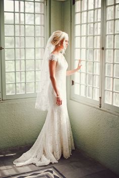 a woman standing in front of a window wearing a wedding dress and holding her hand out