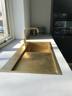 a kitchen sink with a gold faucet in front of a window next to a counter