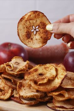 a person is picking up an apple slice from a pile of chips on a cutting board