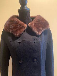 A stylish double breasted winter coat in black. Brown mink collar, which has a hook and eye closure if desired. The pockets are cleverly hidden behind the buttons. The buttons are intact. The lining is free of rips or stains. The mink collar looks like it had been re-sewn at one point. Dan Millstein tag on the inside, as well as the department store it was sold at, Ostereicher's of Salisbury NC. The bust measures 17.5 inches from armpit to armpit laying flat. 39.5 inches from shoulder to hem. Pl Black Winter Pea Coat With Horn Buttons, Vintage Black Outerwear With Horn Royal Buttons, Black Wool Outerwear With Faux Fur Trim, Classic Fur Coat With Padded Collar For Fall, Black Winter Outerwear With Collar, Black Formal Outerwear With Padded Collar, Formal Black Outerwear With Padded Collar, Vintage Black Pea Coat For Winter, Fitted Winter Fur Coat With Padded Collar