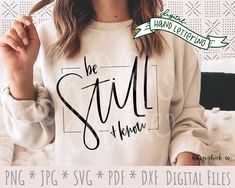 a woman wearing a sweatshirt with the words be still and know in cursive font