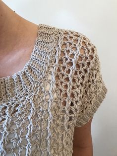 a woman wearing a crochet top with short sleeves and a necklace on her neck