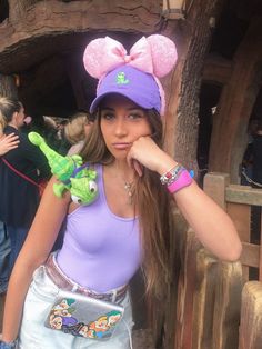 a girl in a purple shirt and hat with a green lizard on her arm, posing for the camera