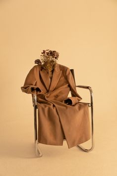 a brown coat sitting on top of a chair with flowers in it's lap