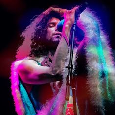 a man with long hair holding a microphone in front of his face while standing on stage