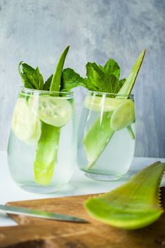 two mason jars filled with cucumber and lime slices on top of a cutting board