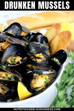 a white bowl filled with mussels next to bread and parsley on the side