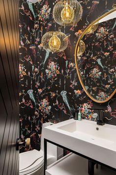 a bathroom with black floral wallpaper and gold lights hanging from the ceiling, along with a white sink