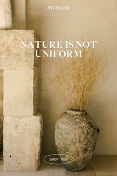 a stone vase with dry grass in it next to a brick wall that says nature is not uniform