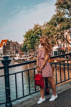 a woman in a red and white checkered dress standing on a bridge looking at the water