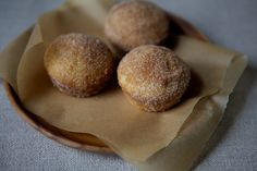 three sugared doughnuts sitting on top of a brown paper in a bowl