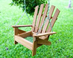 a wooden chair hanging from a chain in the grass with a tree in the background