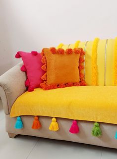 a yellow couch with colorful pillows and tassels on the pillowcase is sitting in front of a white wall