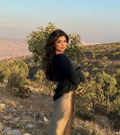 a woman standing on top of a hill next to a tree filled hillside with hills in the background