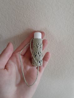 a hand holding a small crocheted object in the shape of a bottle with a chain attached to it