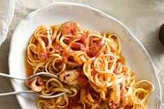 a white plate topped with pasta covered in sauce and meats on top of a table