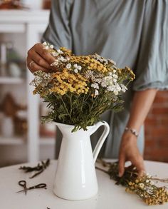 a woman arranging flowers in a white pitcher