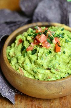 a wooden bowl filled with guacamole and tomatoes