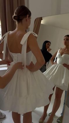 a woman in a white dress looking at herself in the mirror while another person takes a photo