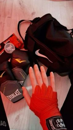 a person's hand with red gloves on top of a wooden table next to a bag